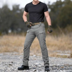 Um homem usando a Calça Tática Masculina RipStop na cor cinza, visto de frente em um cenário árido