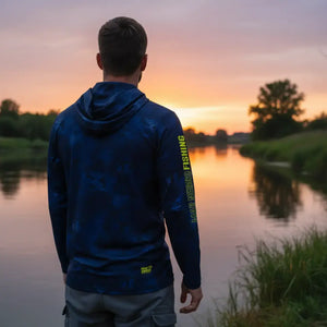Pescador visto de costas usando a Camisa de Pesca Mar Negro Sublimada Capuz Blue, ao fundo tem um rio desfocado
