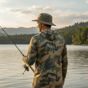 Pescador com chapéu visto de costas segurando uma vara de pesca e usando a Camisa de Pesca Mar Negro Sublimada Capuz Caqui, ao fundo um rio desfocado