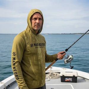 Pescador com capuz visto de frente em cima de um barco segurando uma vara de pesca, usando a Camisa de Pesca Mar Negro Sublimada Capuz Tucuna