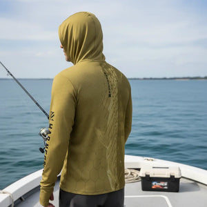 Pescador com capuz visto de costas segurando uma vara de pesca e usando a Camisa de Pesca Mar Negro Sublimada Capuz Tucuna, ao fundo o mar desfocado