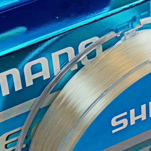 Carretel da Linha Monofilamento Shimano Ultegra Invisitec em zoom, com o foco em seu fio, com a caixa da linha ao fundo