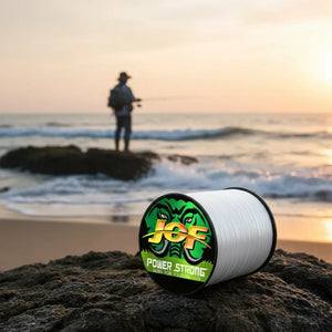 O carretel da Linha Multifilamento JOF 4x na cor branca em destaque em cima de uma pedra, ao fundo um pescador pescando na costeira de uma praia
