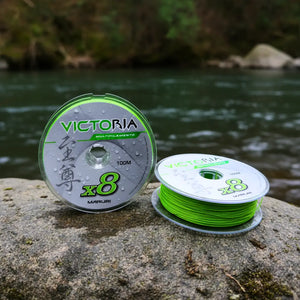 Dois carretéis, um em pé e um deitado da Linha Multifilamento Maruri Victoria 8x na cor verde em cima de uma pedra as margens de um rio