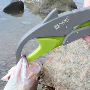 Alicate de Contenção Booms Dolphin cinza com detalhes verde segurando um peixe pela boca as margens de um rio