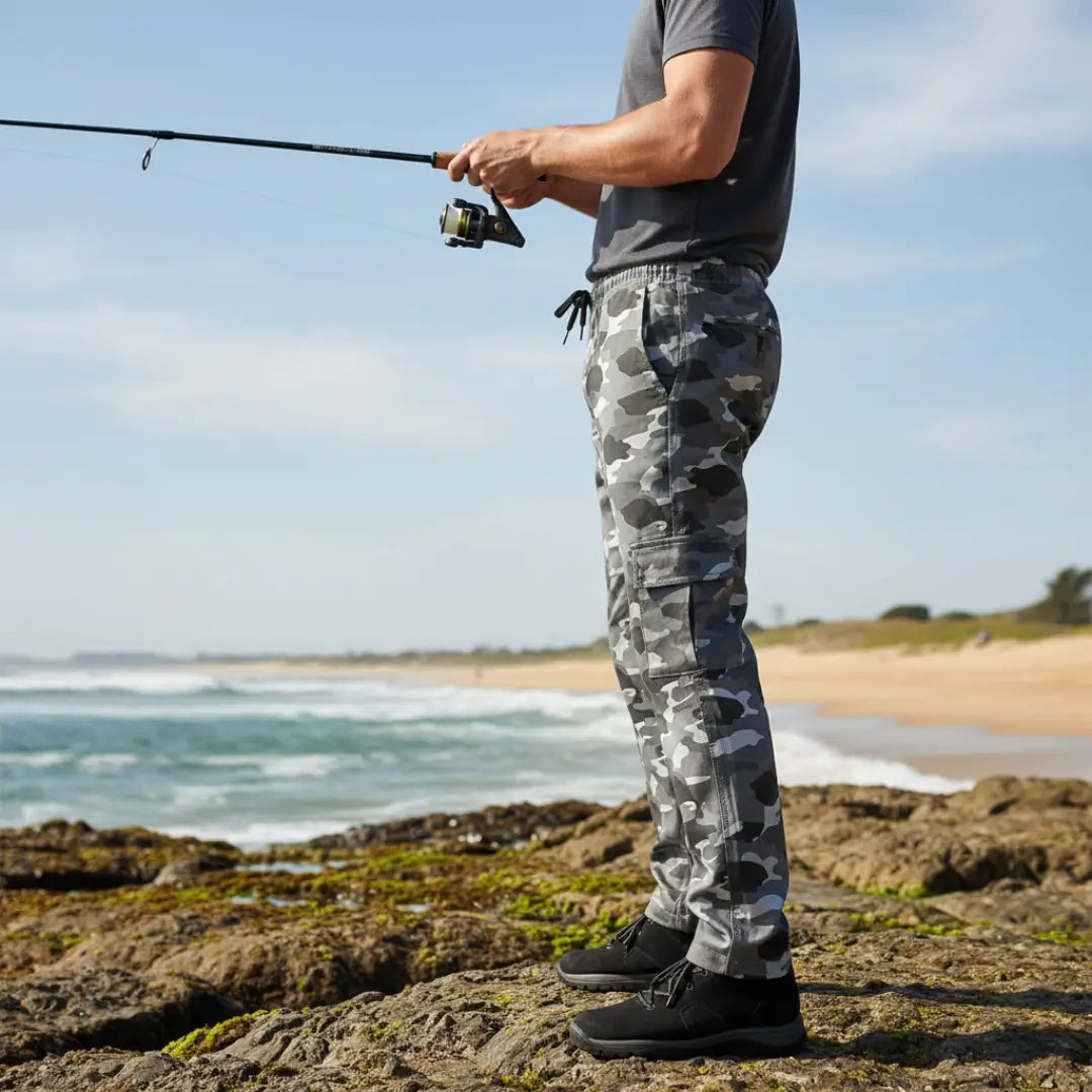 Um pescador visto de lado em uma costeira pescando e usando a Calça Tática Masculina Zanter Camuflada Cinza
