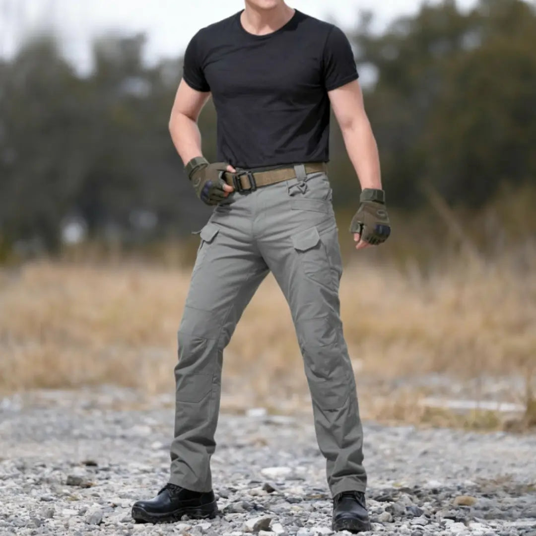 Um homem usando a Calça Tática Masculina RipStop na cor cinza, visto de frente em um cenário árido