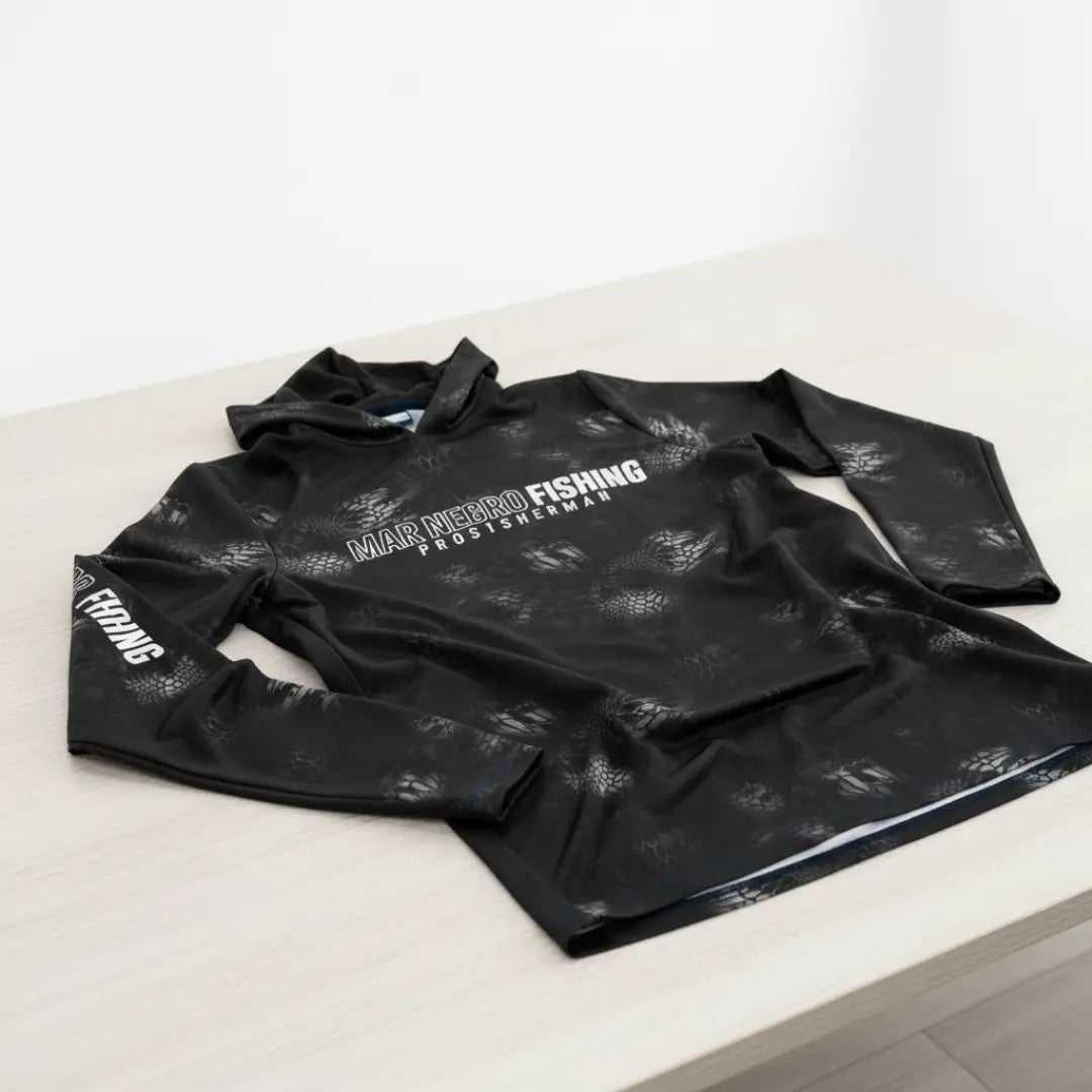 A Camisa de Pesca Mar Negro Sublimada Capuz Black em foco, em cima de uma mesa