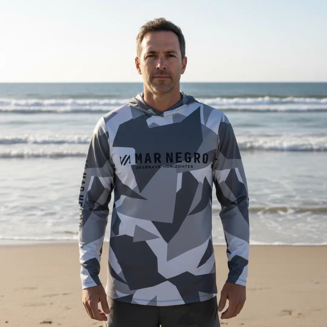 Um pescador visto de frente as margens de uma praia com os braços esticados, usando a Camisa de Pesca Mar Negro Sublimada Capuz Geométrica