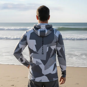 Pescador visto de costas usando a Camisa de Pesca Mar Negro Sublimada Capuz Geométrica, ao fundo o mar desfocado