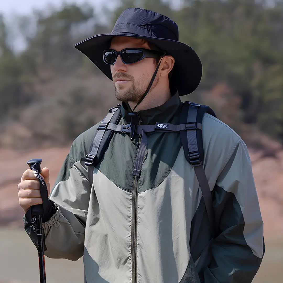 Chapéu de Pesca Zanter Air Field preto usado por um pescador com mochila e bastão, o chapéu apresenta sua aba larga e seu cordão de ajuste no queixo
