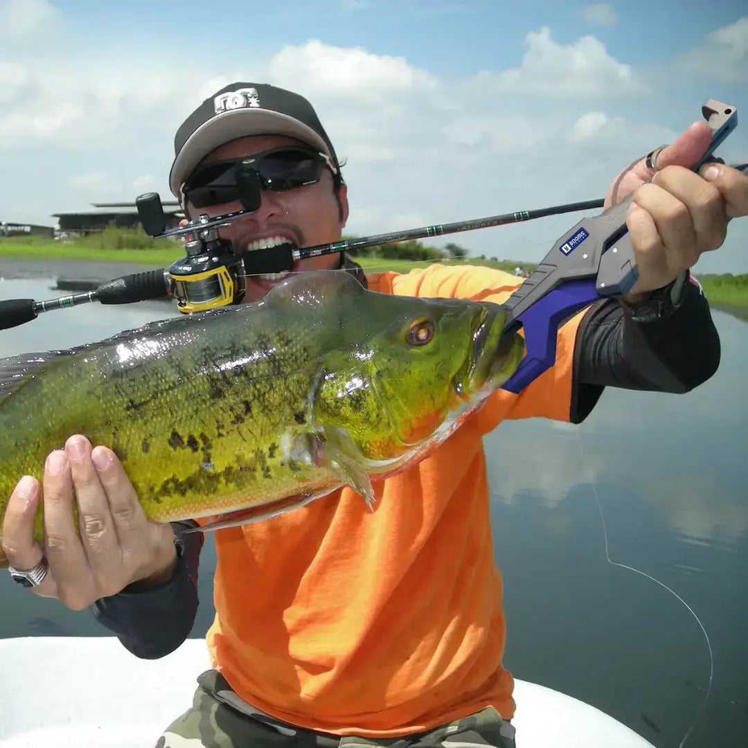 Pescador segurando uma vara de carretilha na boca, e com o alicate de contenção Clamp na boca de um peixe
