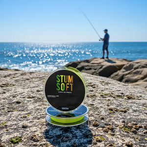 A Linha Monofilamento Albatroz Stum Soft sobre uma pedra na costeira de uma praia, com um pescador em desfoque ao fundo