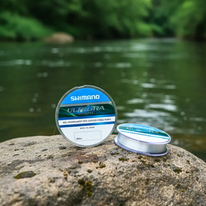 Dois carretéis da Linha Monofilamento Shimano Ultegra Invisitec em cima de uma pedra à beira de um rio, um carretel está em pé e o outro deitado